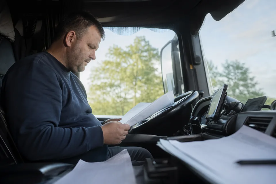 Właściciel małej firmy transportowej przegląda faktury za przewóz w kabinie ciągnika